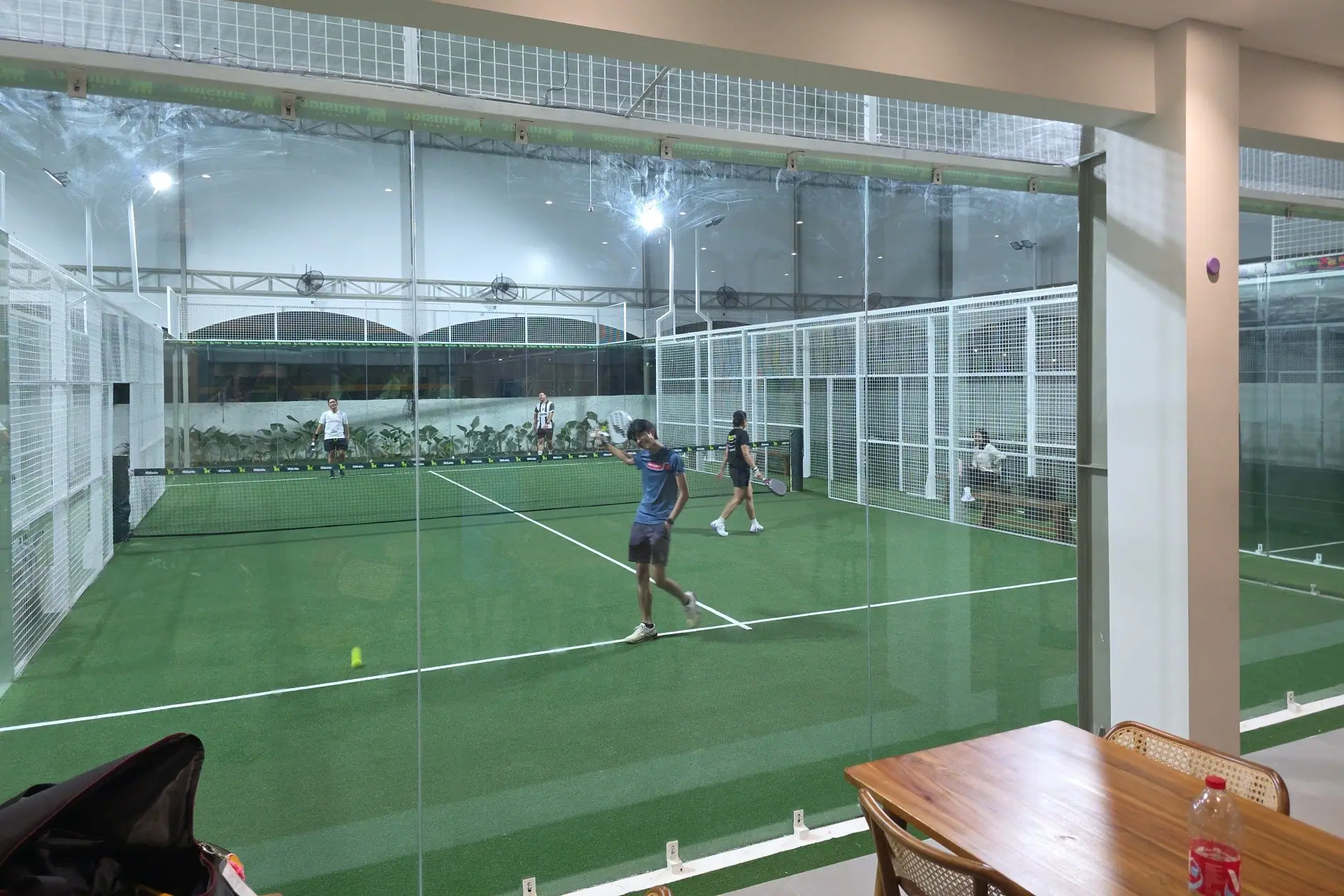 Players on a green court seen through the glass from the café